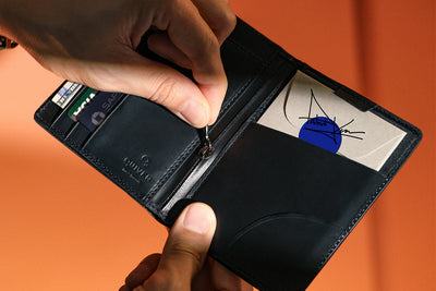 Person opening a black wallet with a visible brand logo on an orange background